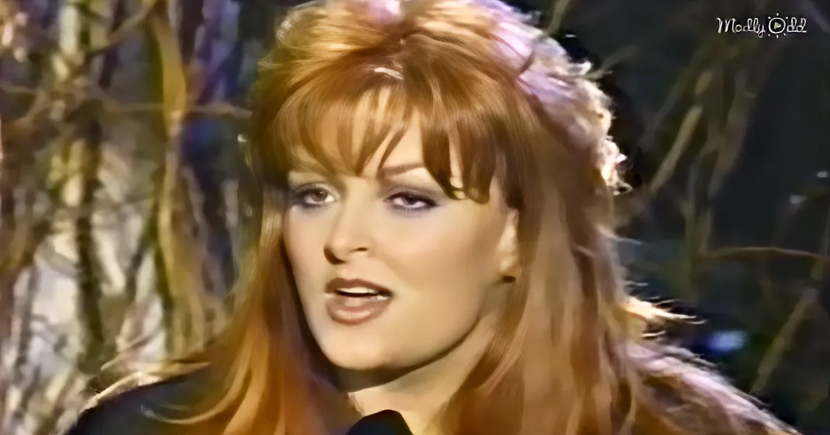 A woman with long, wavy red hair and bangs is singing into a microphone.
