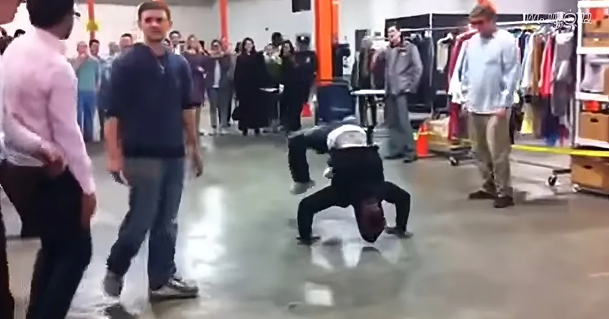 A person performs a handstand in a room with spectators watching.