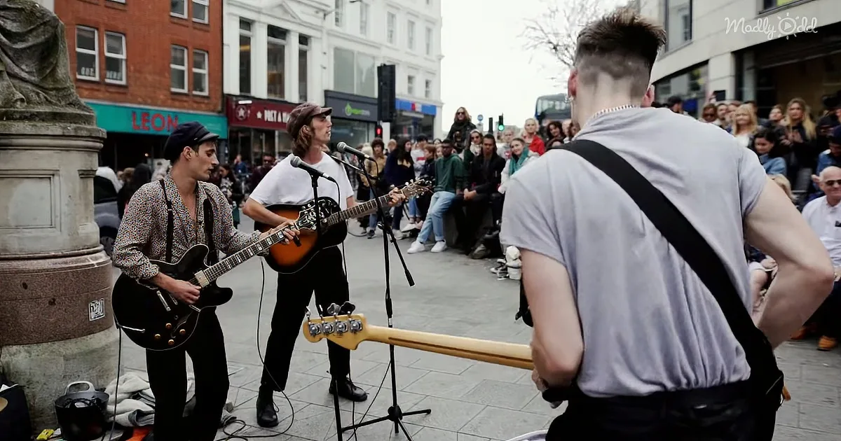 A street performer plays guitar while a crowd watches in a city square.