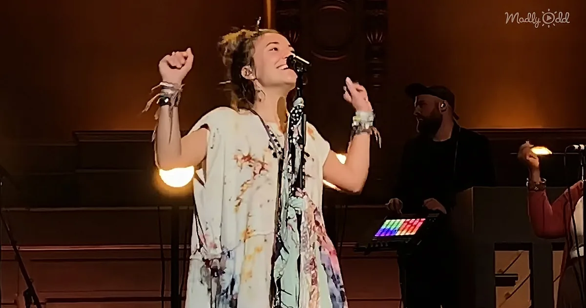 A woman in a floral dress sings passionately on stage, raising her fist in the air.