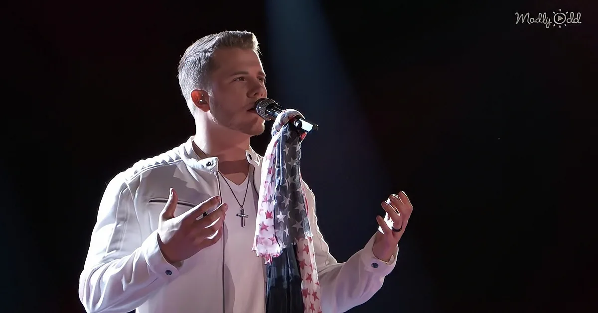 A man in a white jacket sings into a microphone, adorned with a scarf, against a dark background.