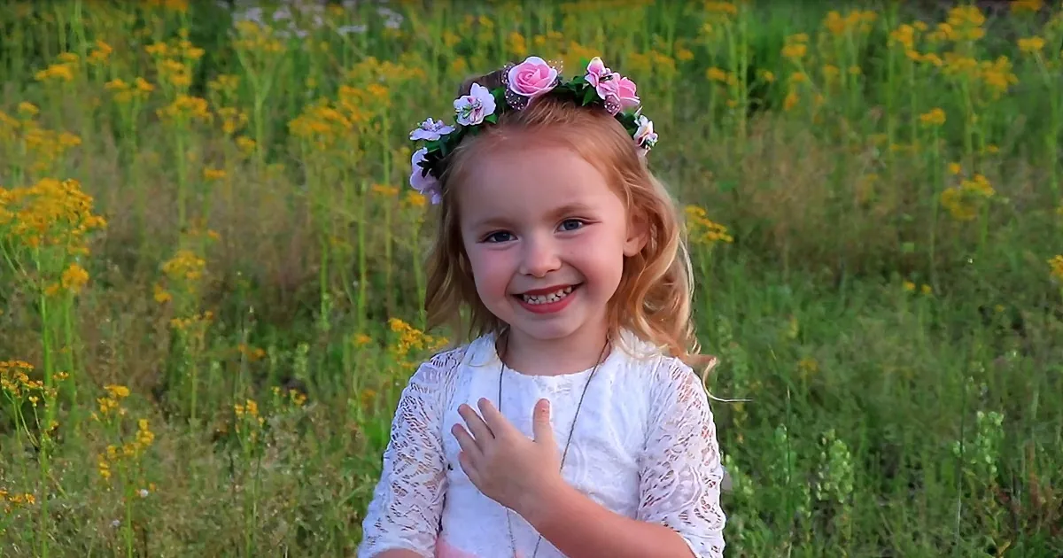 A smiling child with a flower crown sits in a field of yellow flowers.