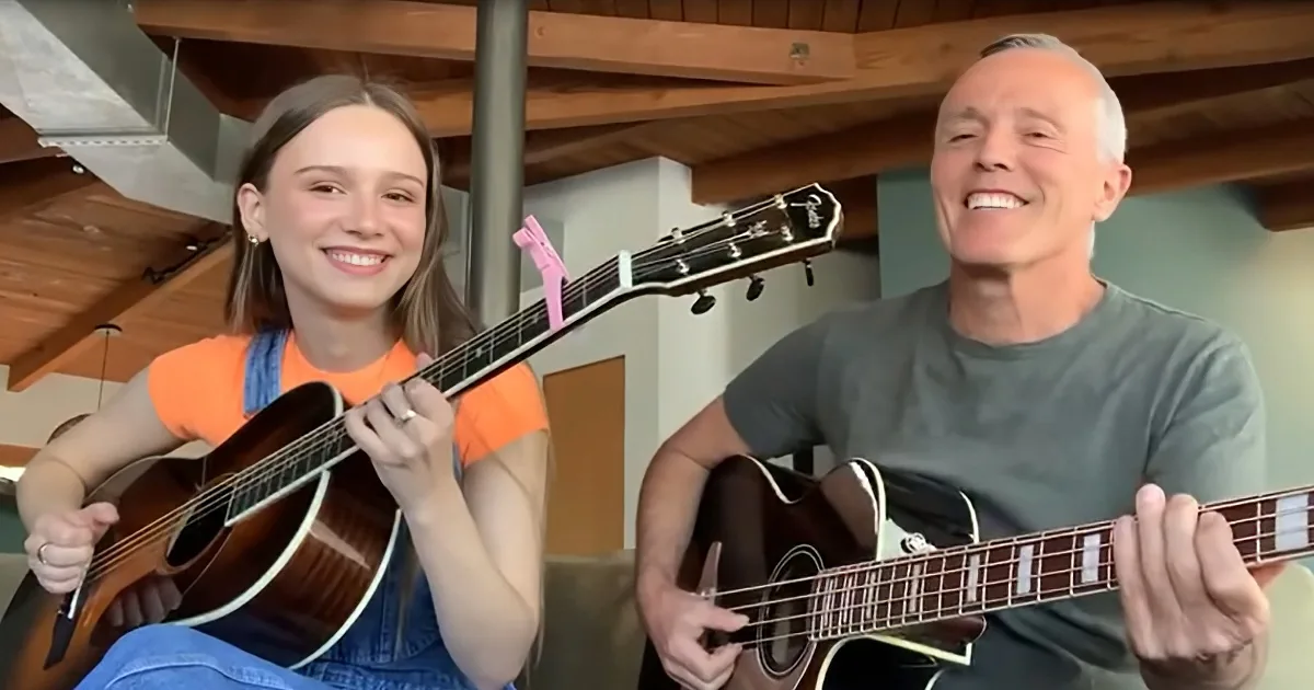 A young girl and an older man smile while playing guitars together in a cozy room.