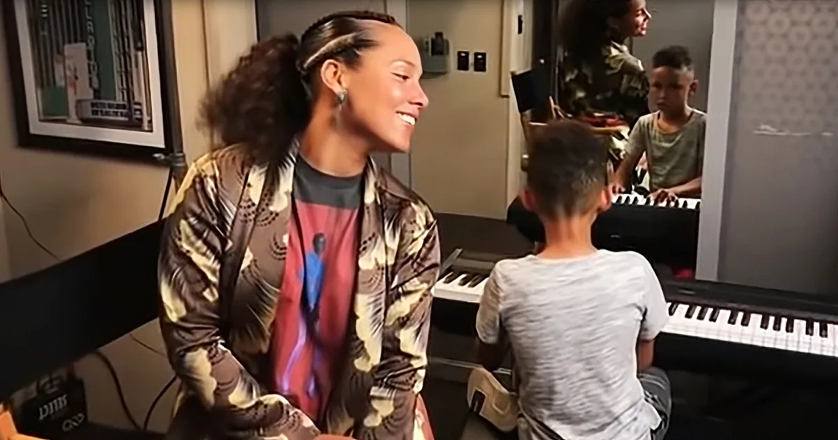 A woman smiles while a boy plays piano in a music studio.