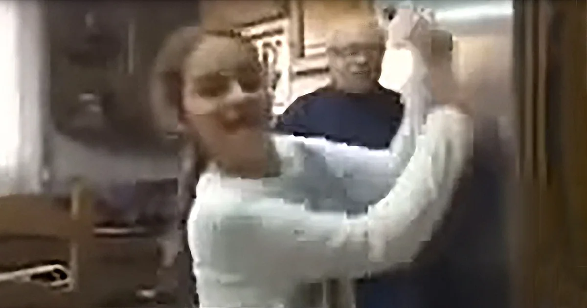 A person in a white outfit is being held up by another person in a kitchen setting.