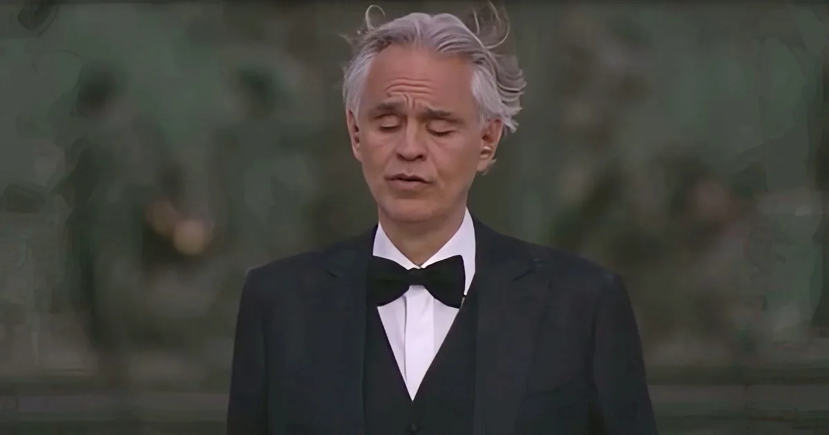 A man with gray hair in a black tuxedo and bow tie stands in front of a blurred background.