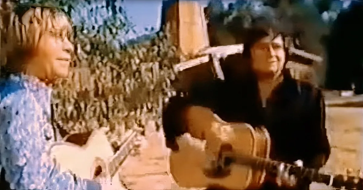 Two individuals, one playing guitar, sit outdoors with a scenic background.