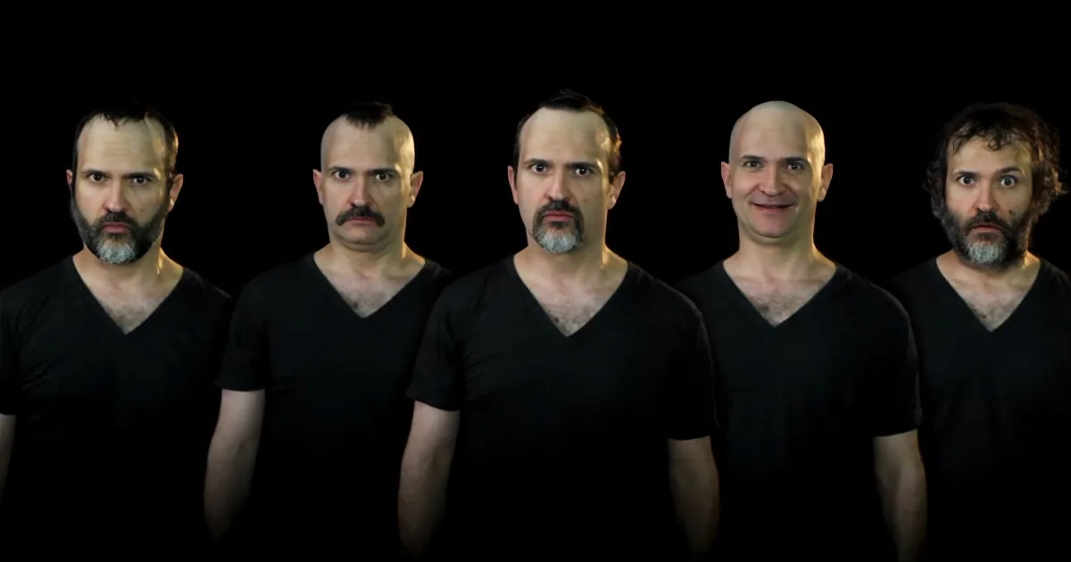 Five men in black V-neck shirts stand in a row against a dark background.