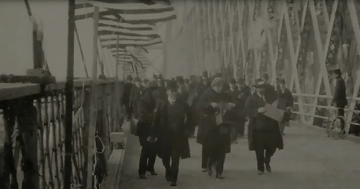 A crowd of people in formal attire walks under a bridge adorned with American flags.