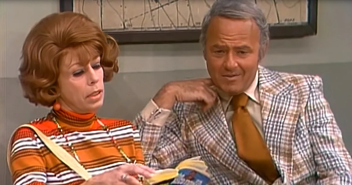 A woman in a striped shirt and a man in a checkered suit are looking at a book together.