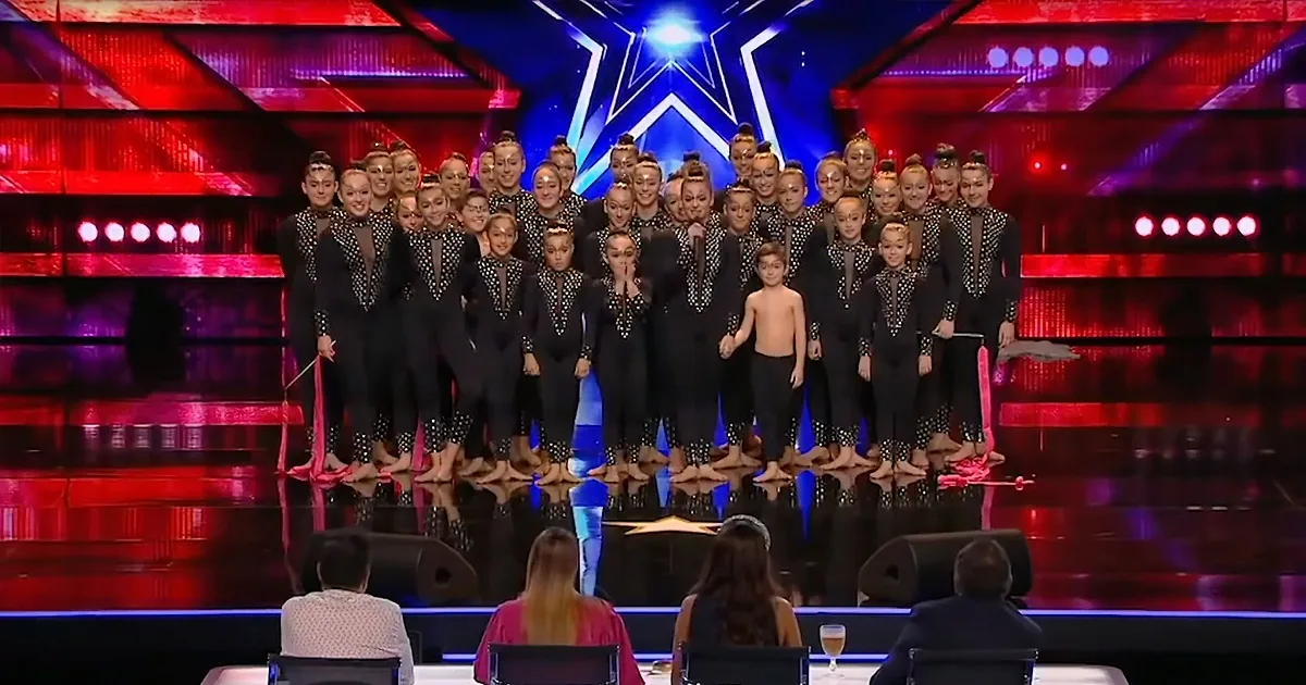 A group of performers in black outfits stands on a stage with a bright star backdrop, posing for a photo.