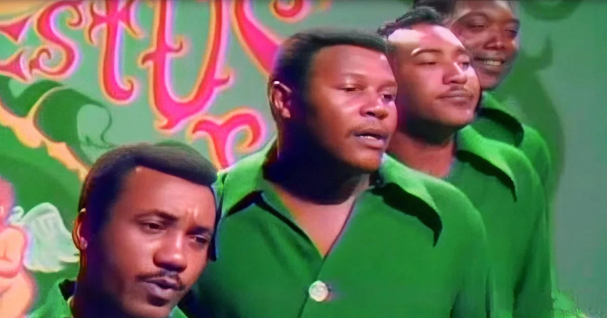 A man in a green shirt sings with a group, surrounded by colorful background.