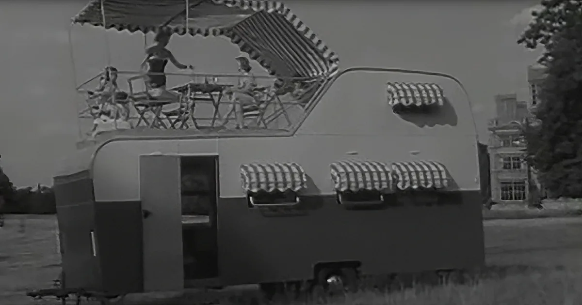 A vintage camper with striped awnings and people enjoying a meal on its roof.