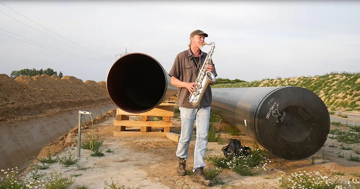A man plays saxophone next to a large pipe in a construction site.