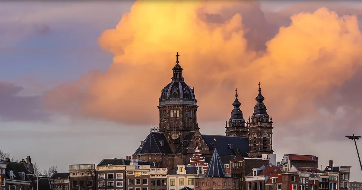 A grand church with a domed roof and spires stands against a dramatic sky with orange clouds.