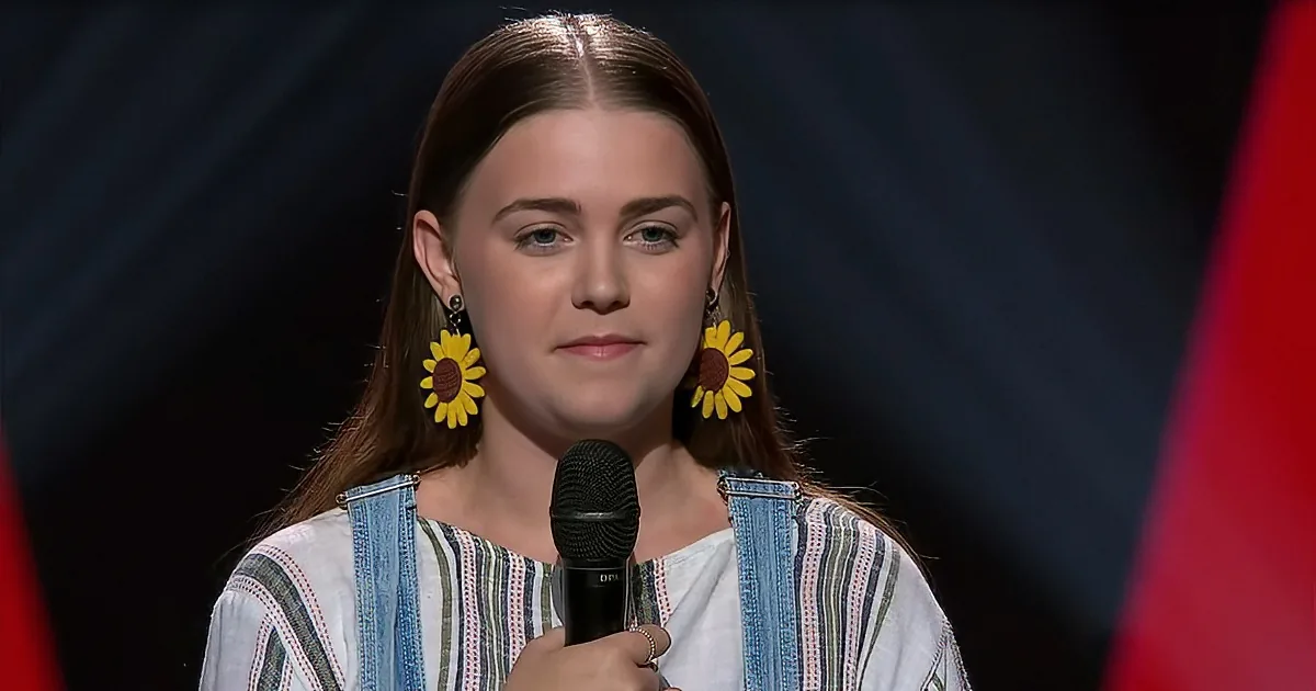 A person wearing a striped shirt and sunflower earrings holds a microphone, standing against a dark background.