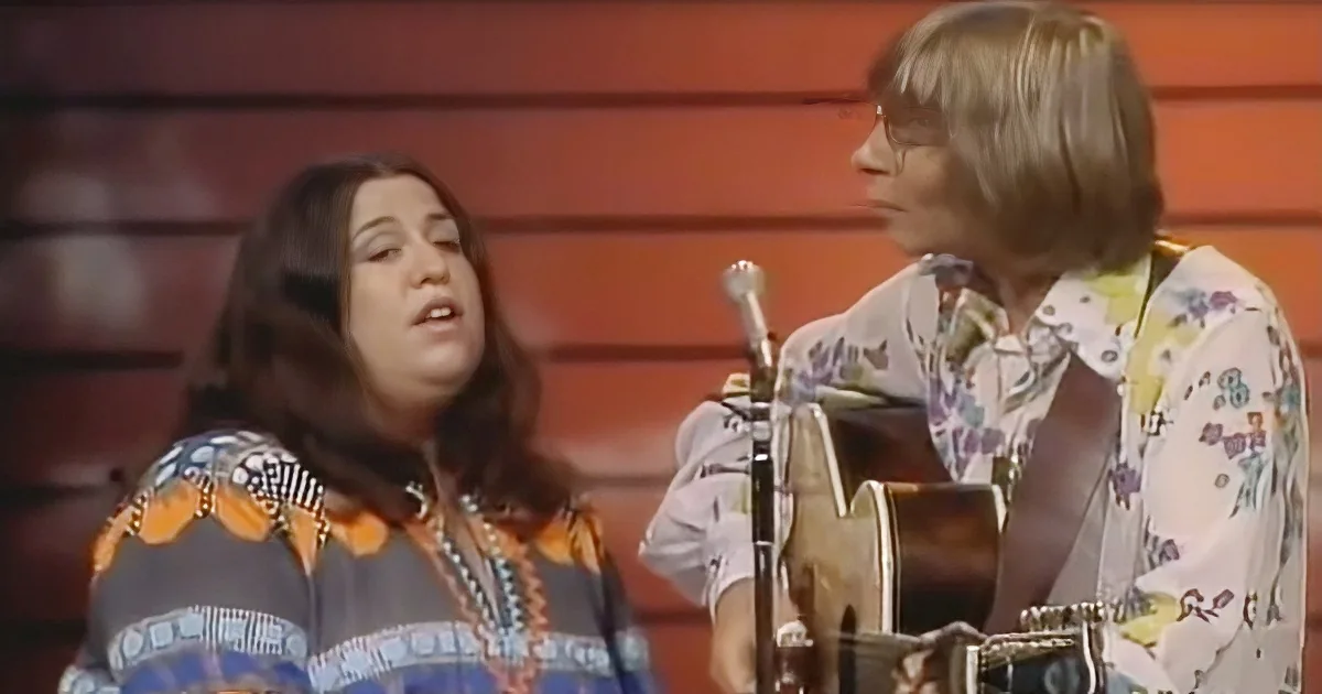 A woman in a colorful patterned shirt sings while another person plays guitar, both in a studio setting.