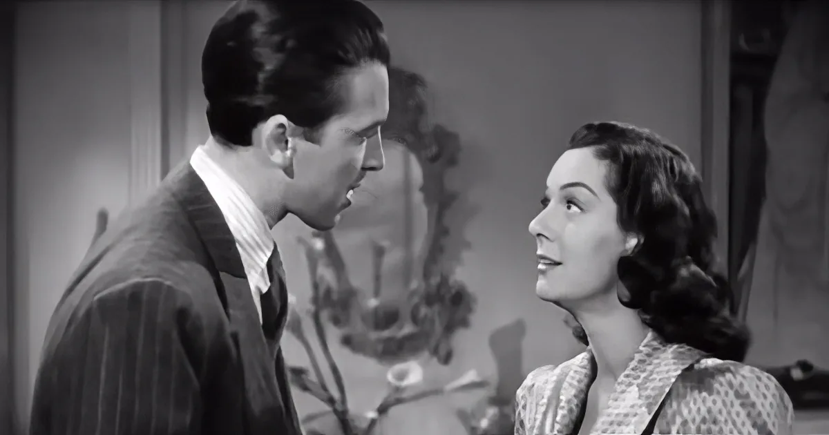 A man and woman are facing each other, seemingly engaged in a conversation in a vintage setting.