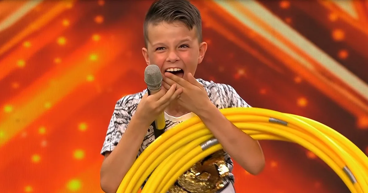 A boy with a microphone and a yellow hula hoop smiles enthusiastically on a vibrant orange background.