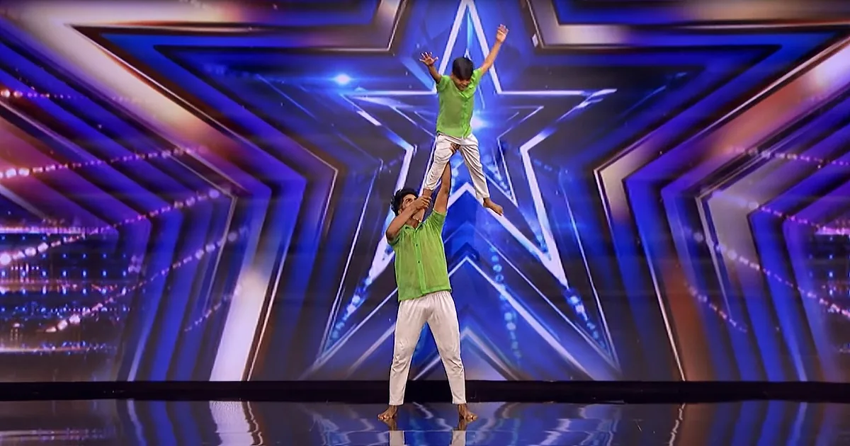 A man lifts a child in the air on a stage with a star backdrop.