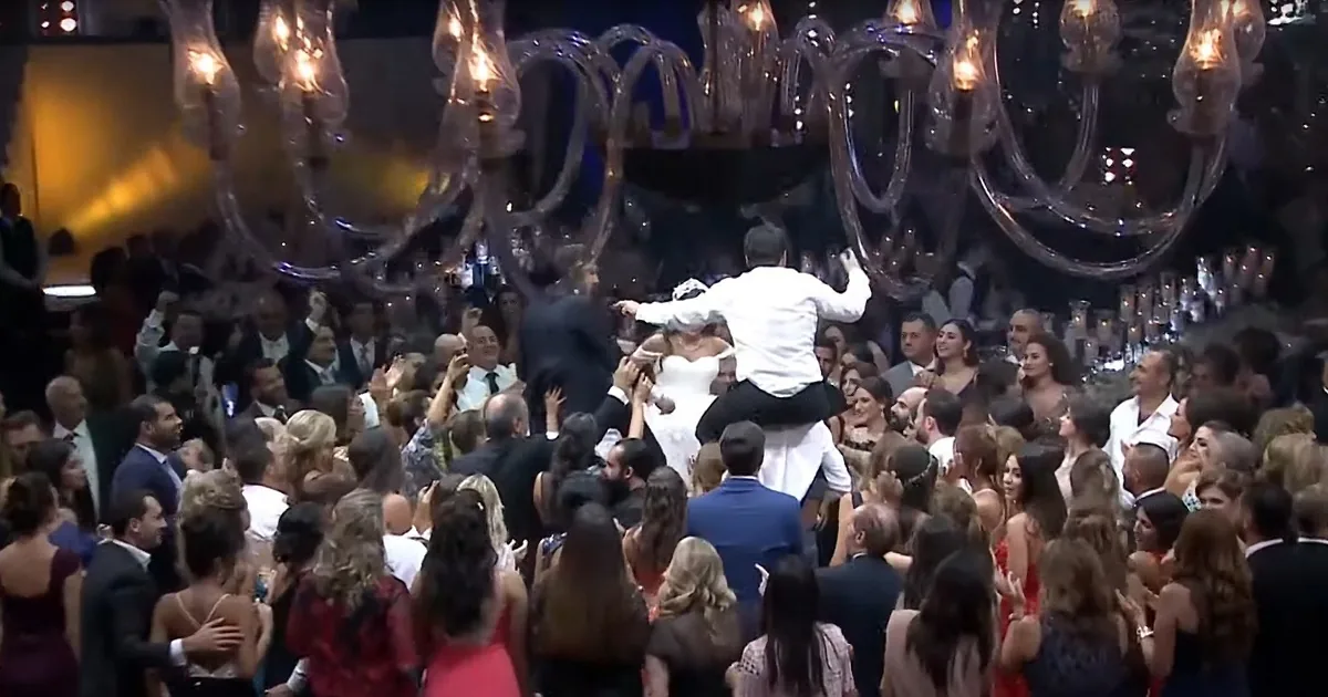 A man lifts a woman in a white dress above a crowd at a formal event.