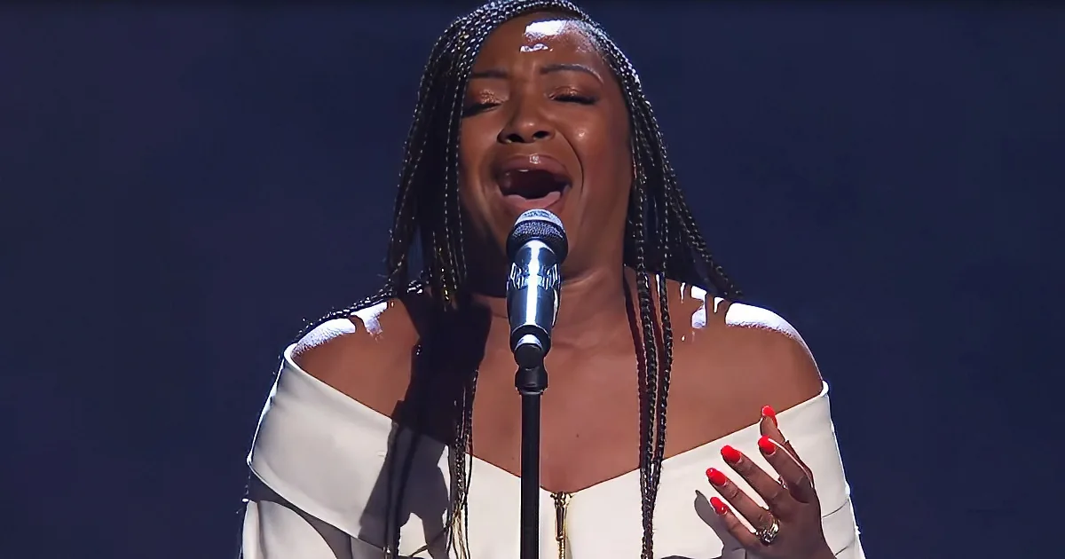 A woman in a white off-shoulder dress sings passionately into a microphone, her hands adorned with red nail polish.