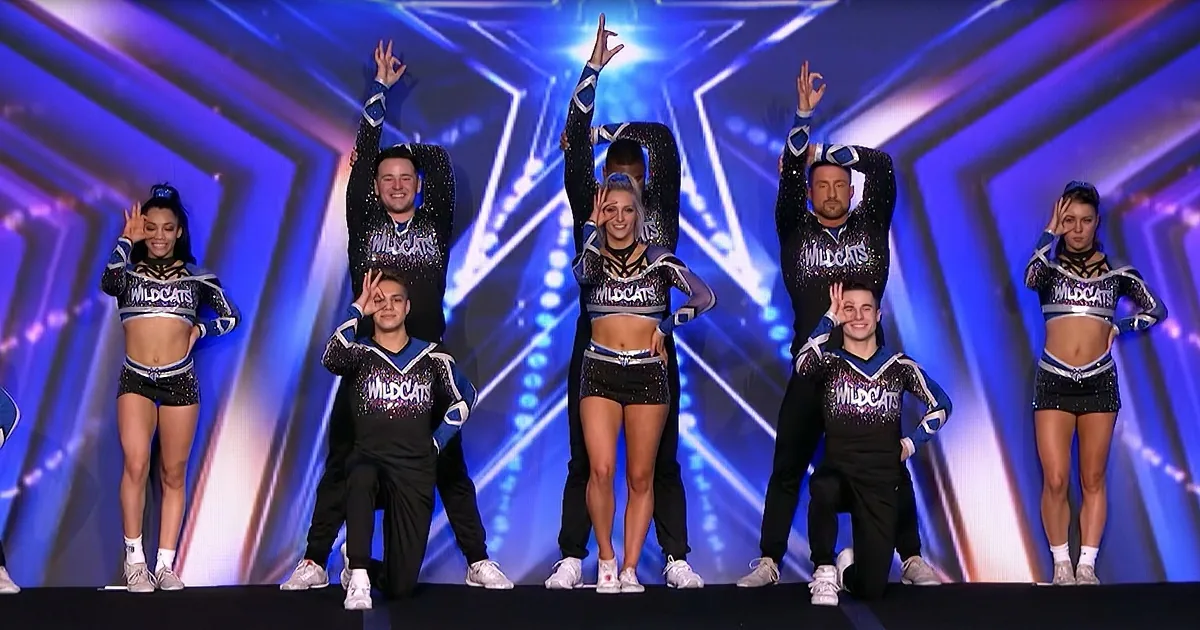 Cheerleaders in "Wildcats" uniforms perform a synchronized routine on a stage with a blue star background.