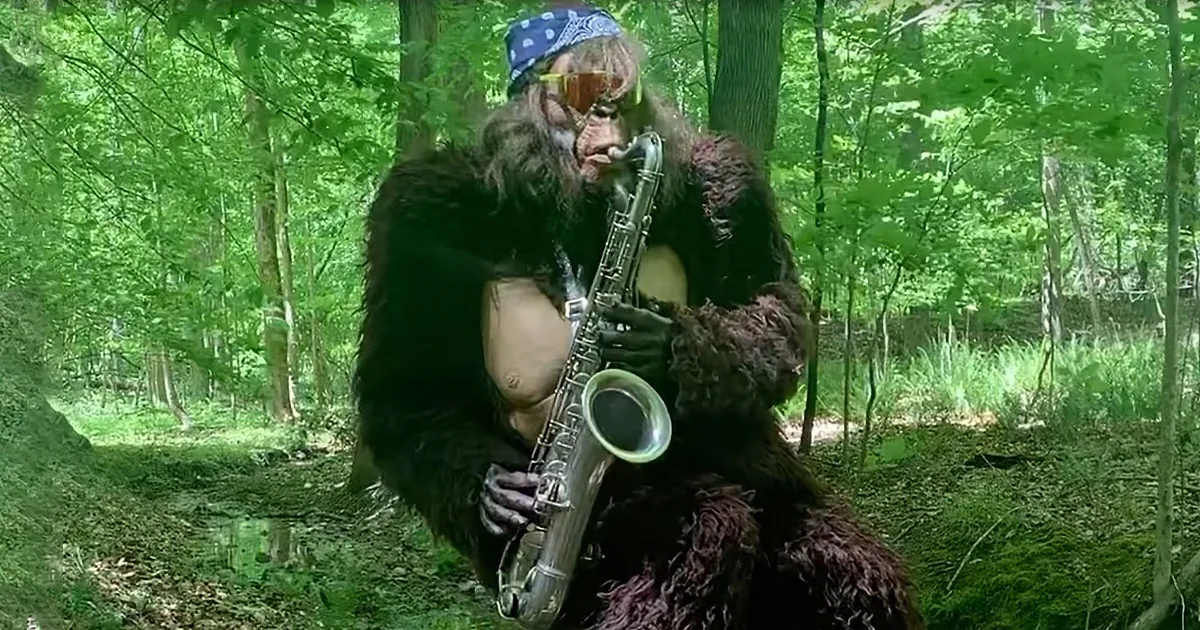 A person in a furry costume plays a saxophone in a lush green forest.