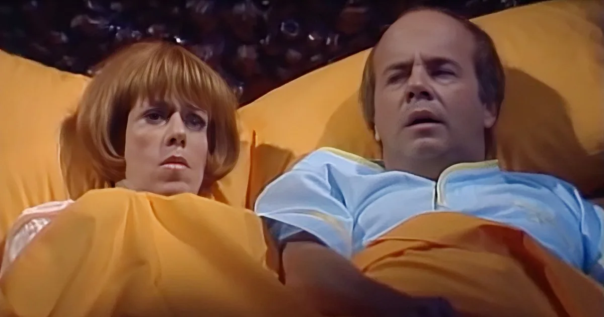 A woman with short red hair and a man in a light blue shirt are lying down, possibly in a spaceship, with a yellow...