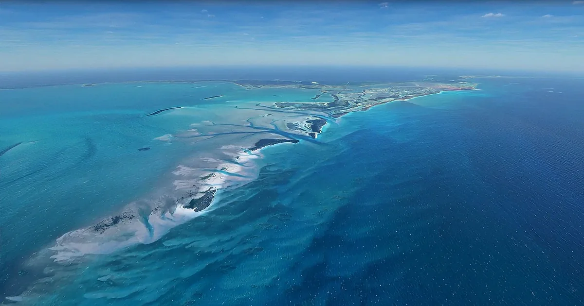 Aerial view of turquoise waters with sandbars and islands, under a clear blue sky.