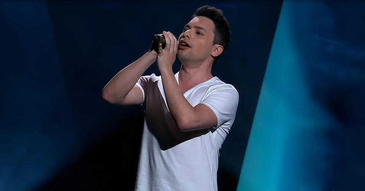 A man in a white shirt sings passionately into a microphone on stage.