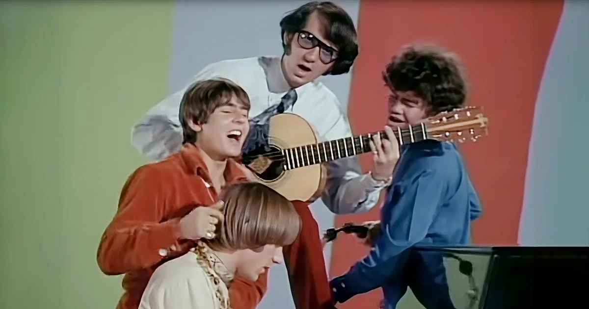 A group of young men, one playing guitar, another singing, and a third holding a microphone, perform together on stage.