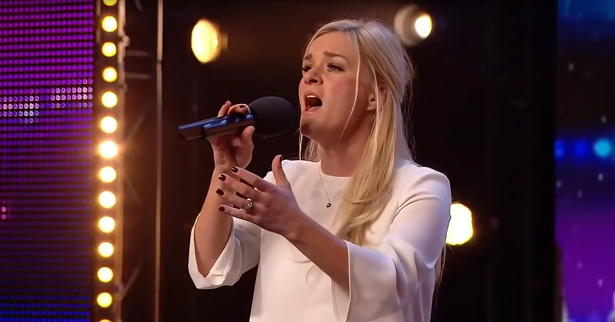A woman in white sings passionately into a microphone on stage with colorful lights.