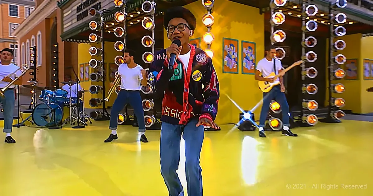 A person sings into a microphone on a brightly lit stage with a band and colorful background.