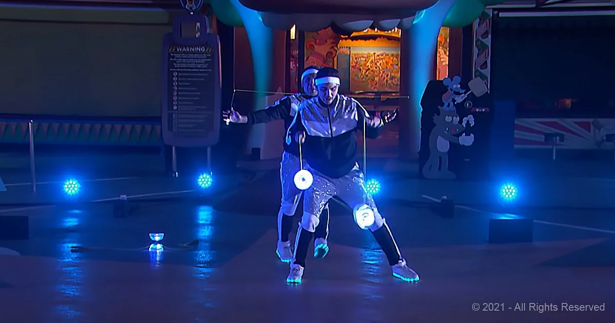 A person in a silver outfit performs a dance routine with glowing objects, illuminated by blue stage lights.