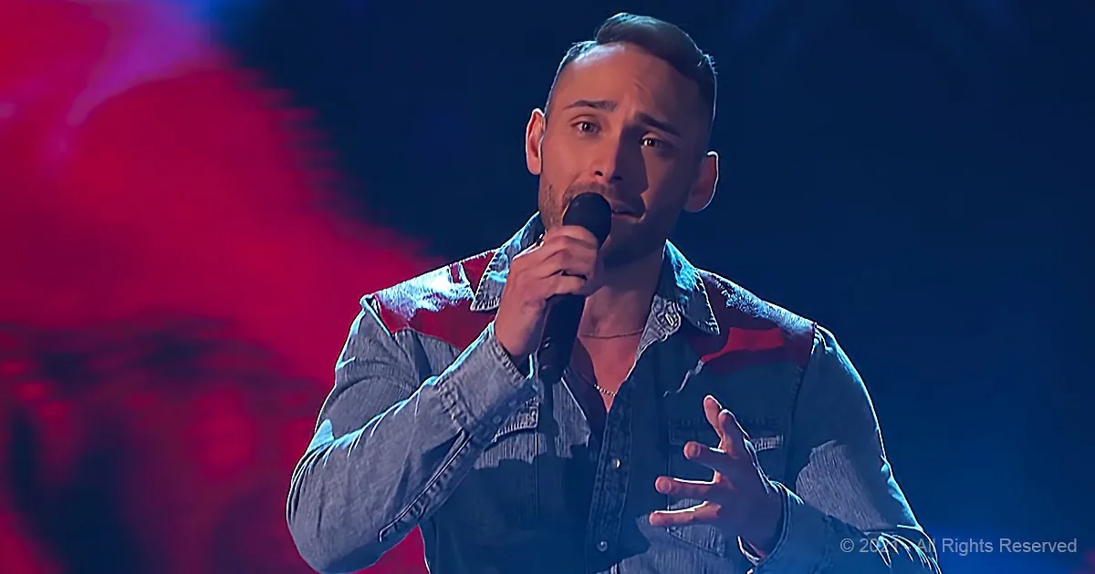 A man in a denim shirt sings into a microphone, gesturing with his hands.