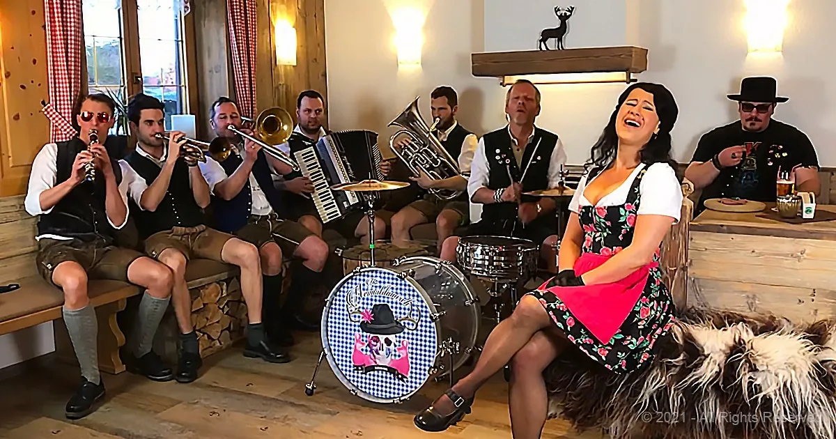 A woman in a dirndl sings while a band in traditional German attire plays music in a cozy room.