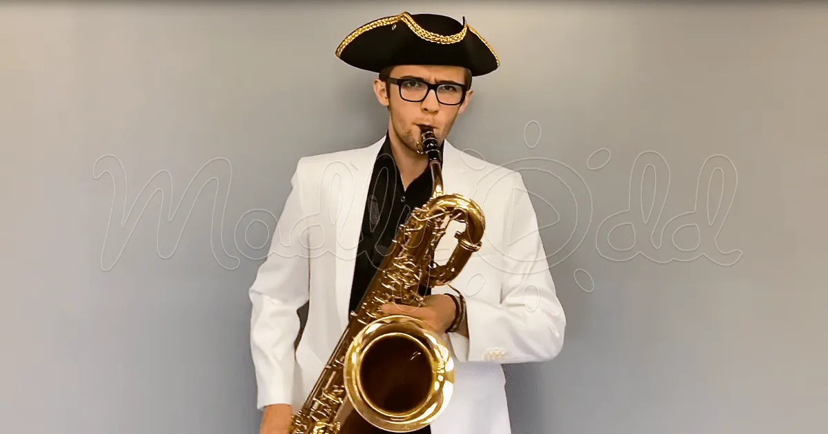 A man in a white suit and tricorn hat plays a saxophone against a plain background.