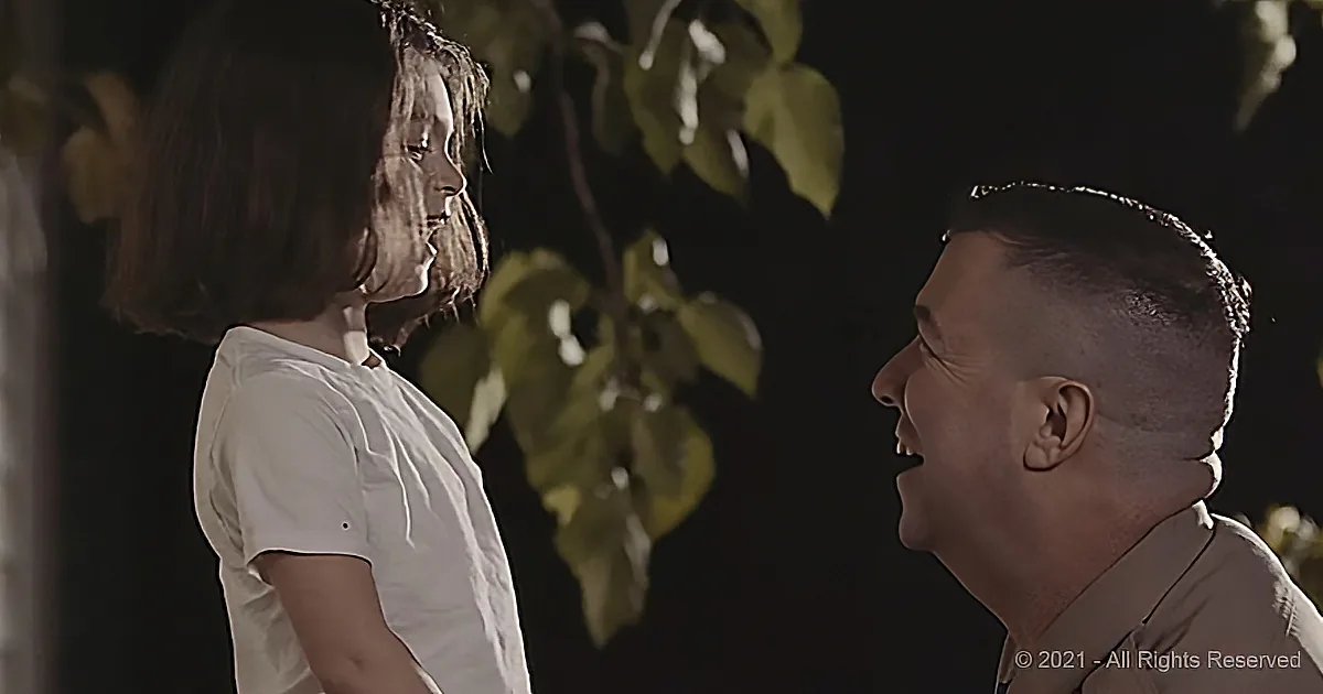 A man and a young girl are facing each other, both smiling, with leaves in the background.