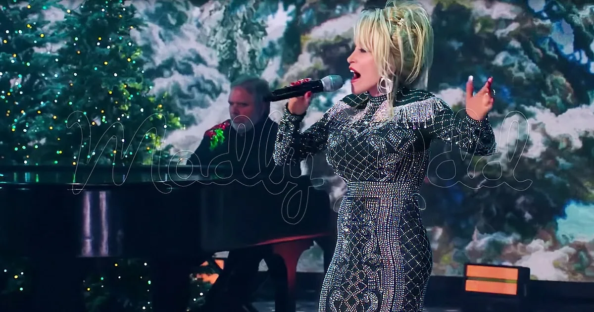 A woman in a sparkly dress sings into a microphone, with a Christmas tree and snowy backdrop behind her.