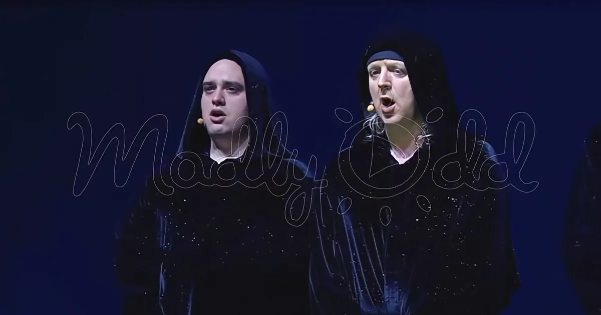 Two individuals in dark costumes with hoods, possibly performing on stage, with a dark background.
