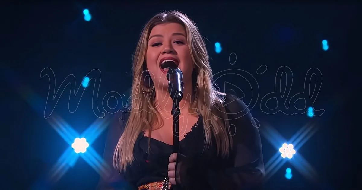 A woman sings into a microphone on stage with blue lights and a "Maisy Didd" watermark.