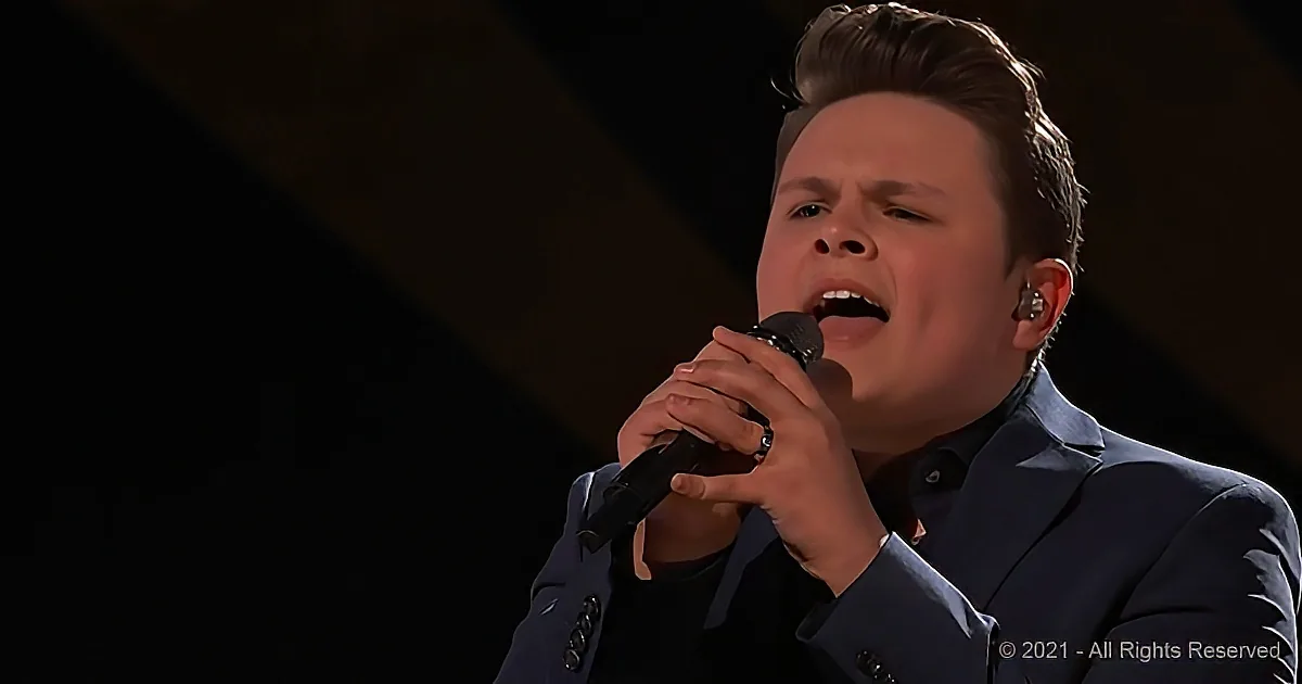 A man in a dark suit sings passionately into a microphone, wearing an earpiece.
