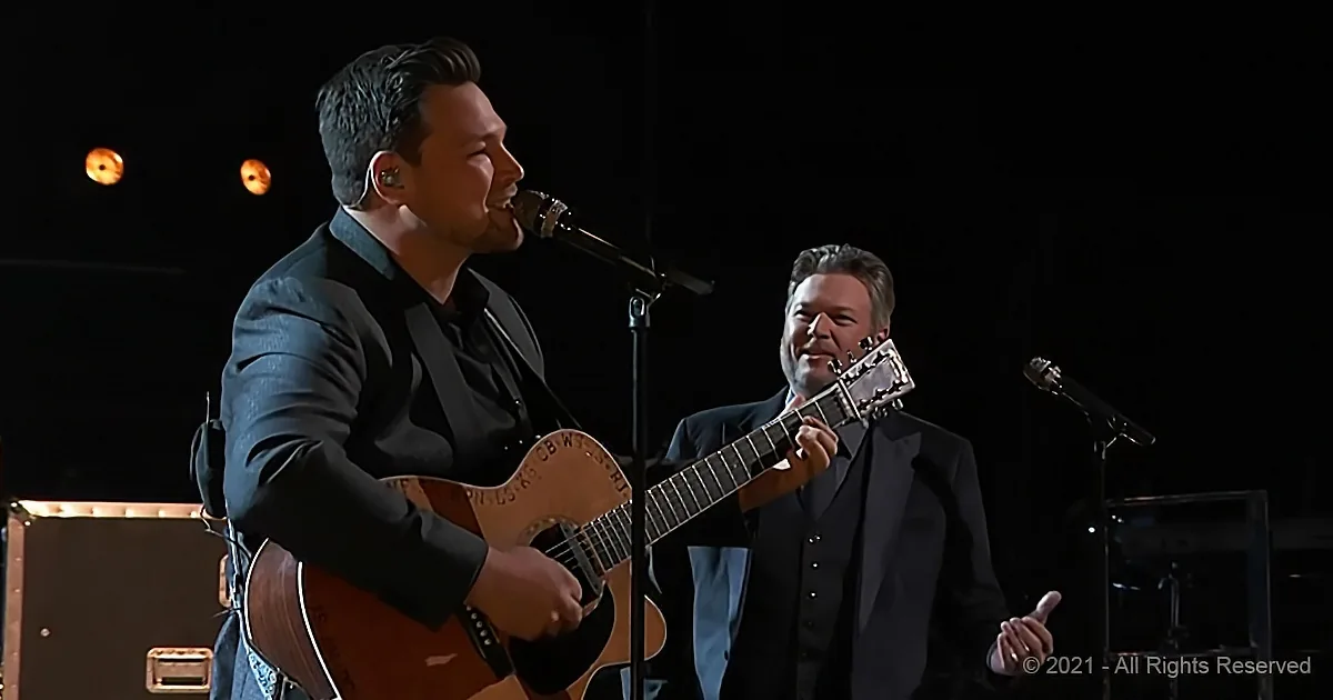 A man in a suit plays guitar while another man in a suit sings into a microphone.