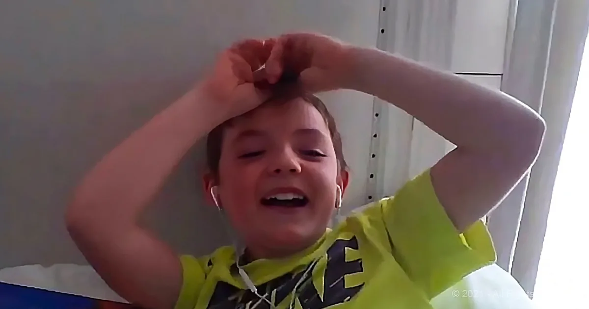 A child in a yellow shirt makes a heart shape with their hands while smiling.