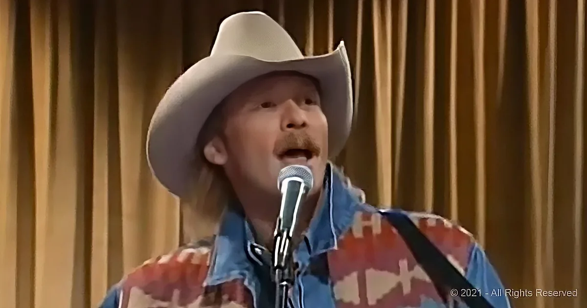 A man in a cowboy hat and plaid shirt sings into a microphone.