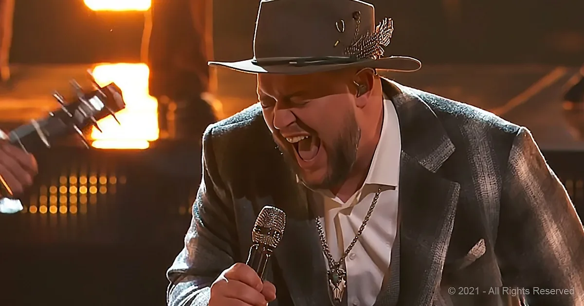 A man in a hat and suit sings passionately into a microphone on stage.