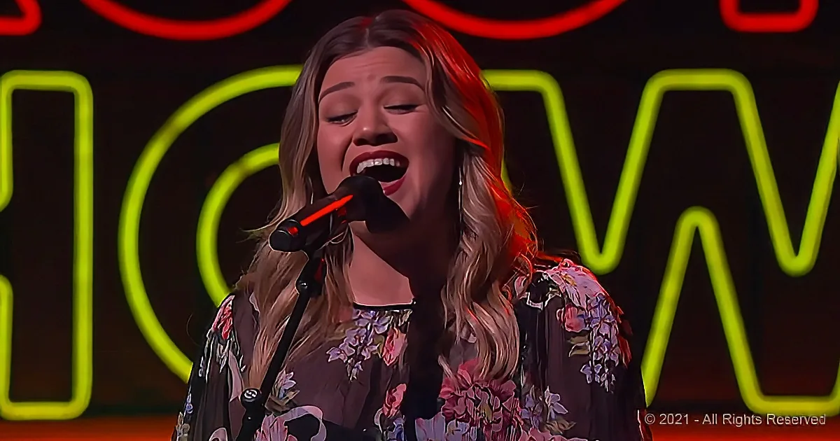 A woman sings passionately into a microphone, wearing a floral top, with neon "HOW" lights in the background.