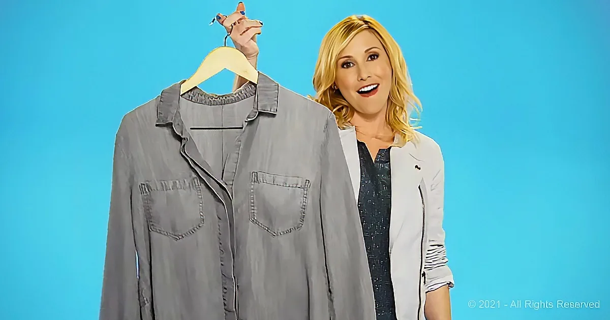 A woman holds a gray shirt on a hanger, smiling against a blue background.