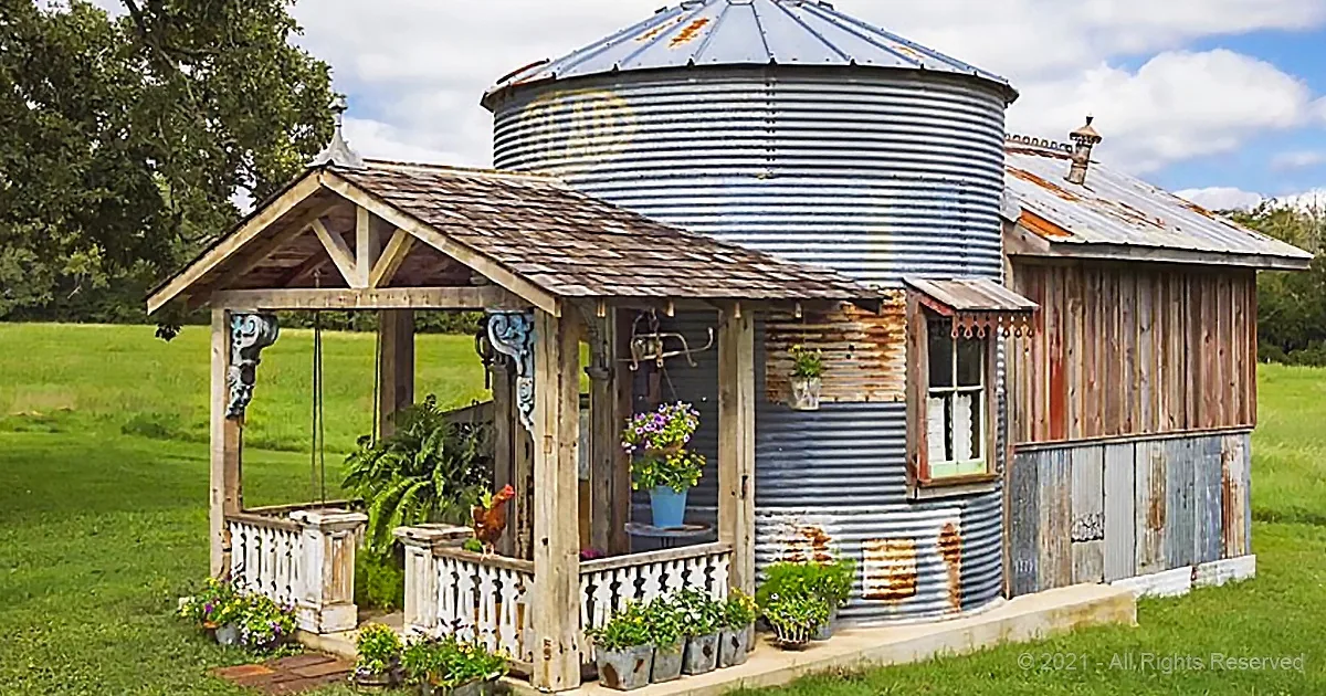 A rustic, weathered grain silo repurposed into a charming outdoor living space with plants and a swing.